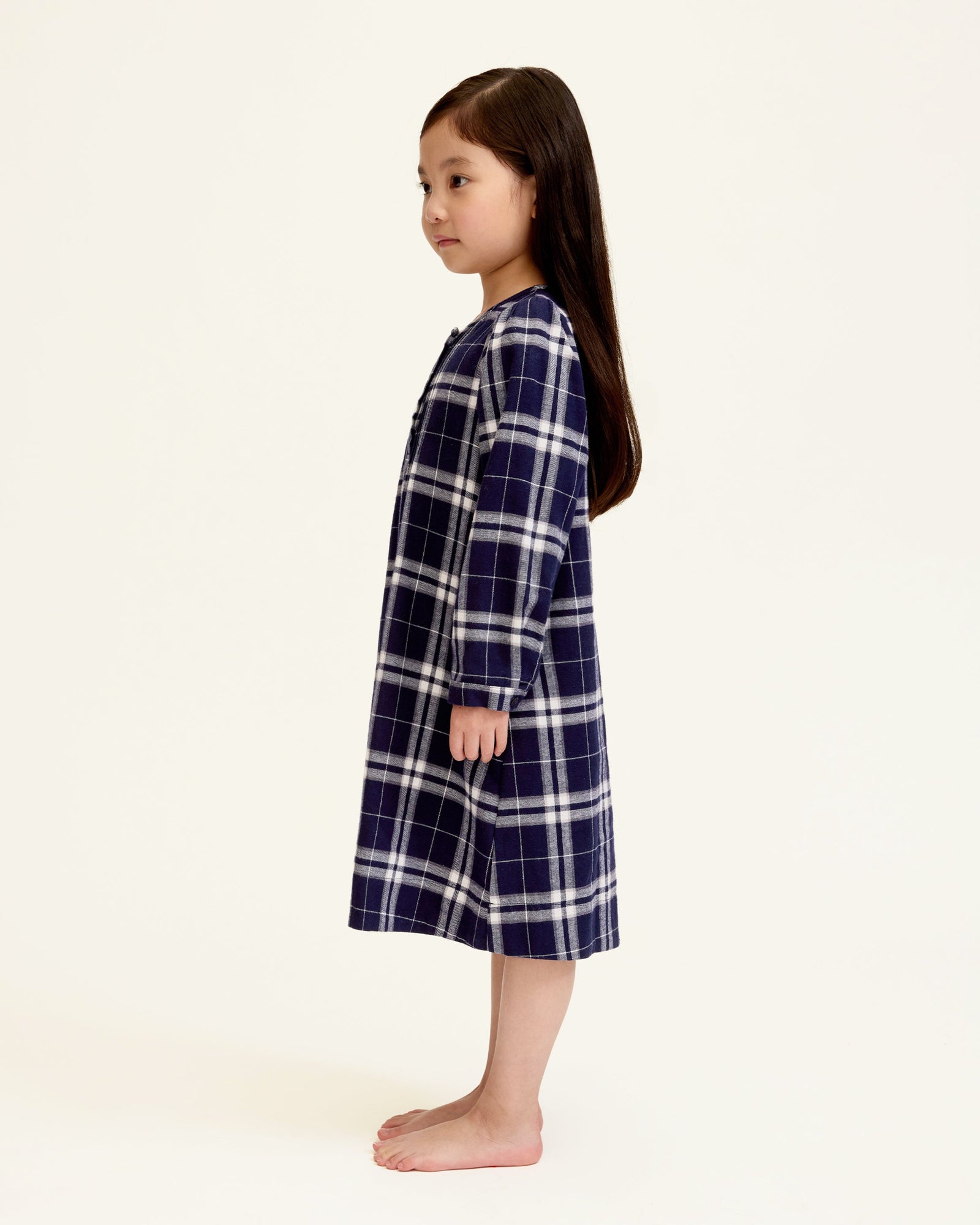 The Girl's Brushed Twill Beatrice Nightgown in Oxford Tartan features a navy, white, and gray plaid pattern, long sleeves, a round neckline, front buttons, and pleats near the chest.