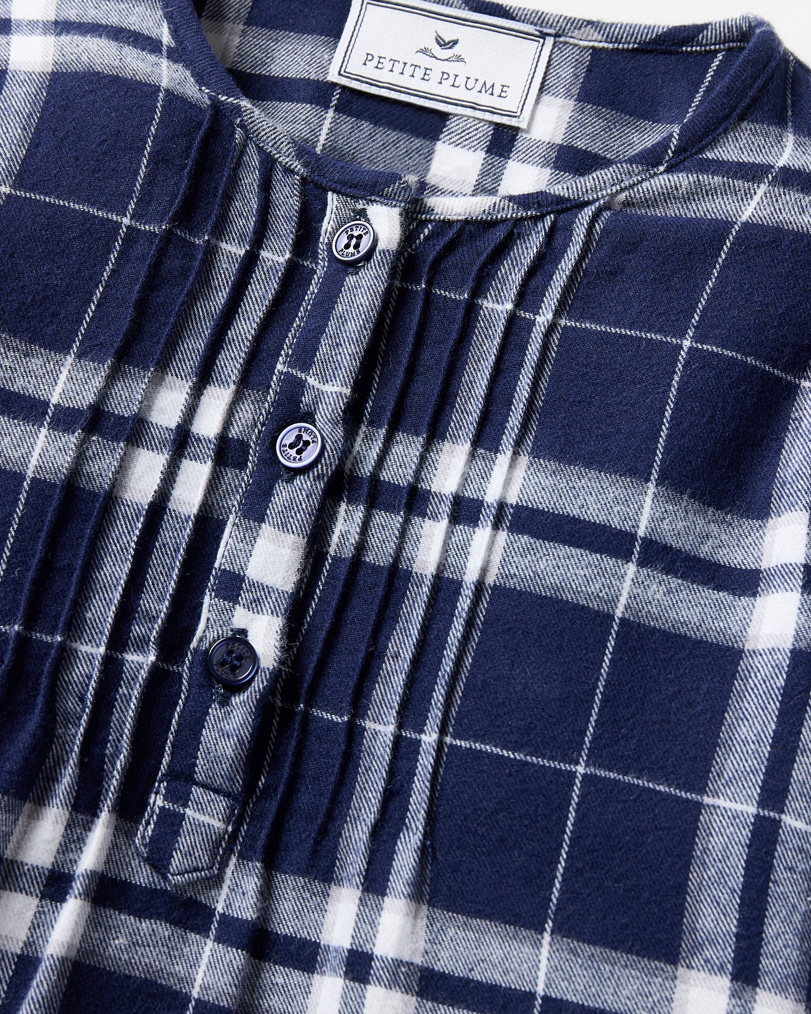 The Girl's Brushed Twill Beatrice Nightgown in Oxford Tartan features a navy, white, and gray plaid pattern, long sleeves, a round neckline, front buttons, and pleats near the chest.