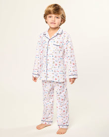 The Kid's Twill Pajama Set in Literary Lessons features a white collared, long-sleeve button-up top and matching pants with a colorful school-themed pattern and navy blue piping accents.