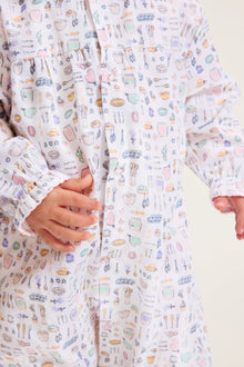 The Baby's Twill Madeline Romper in Baking Spirits Bright features long sleeves, a ruffled collar and cuffs, pastel kitchen print on white, front buttons, and snap closures at the legs for easy dressing.