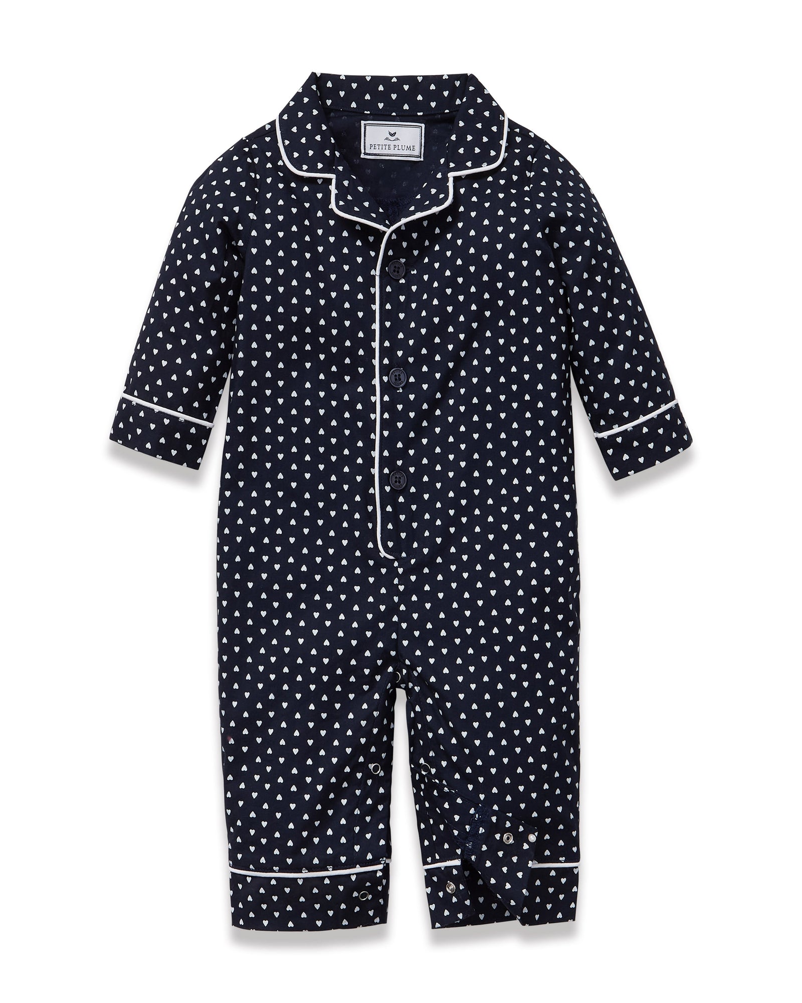 The Baby's Twill Classic Romper in Midnight Hearts is a navy blue onesie with long sleeves and legs, featuring a white heart pattern and white piping on the collar, cuffs, and front.