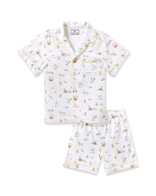 Two smiling children in luxurious Petite Plume sleepwear sit on the floor. They sport matching Kids Twill Short Sets in an Easter Frolic print. One child cuddles a stuffed bunny, embodying comfort and joy against a plain backdrop.