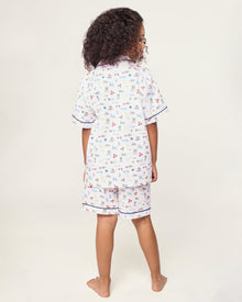 The Kid's Twill Short Set in Literary Lessons features a white base with colorful school-themed prints—pencils, books, and erasers—plus navy piping on the collar, pocket, sleeves, and shorts.