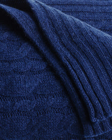 The Petite Plume Cashmere Cable Knit Throw in Navy showcases a textured cable-knit pattern and ribbed edges for a luxurious touch to your decor.
