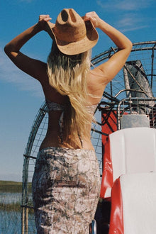 Woman wearing camouflage print skirt with black sleeveless top, viewed from behind outdoors.