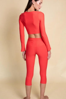 Woman wearing a red long-sleeve crop top and matching red capri leggings.