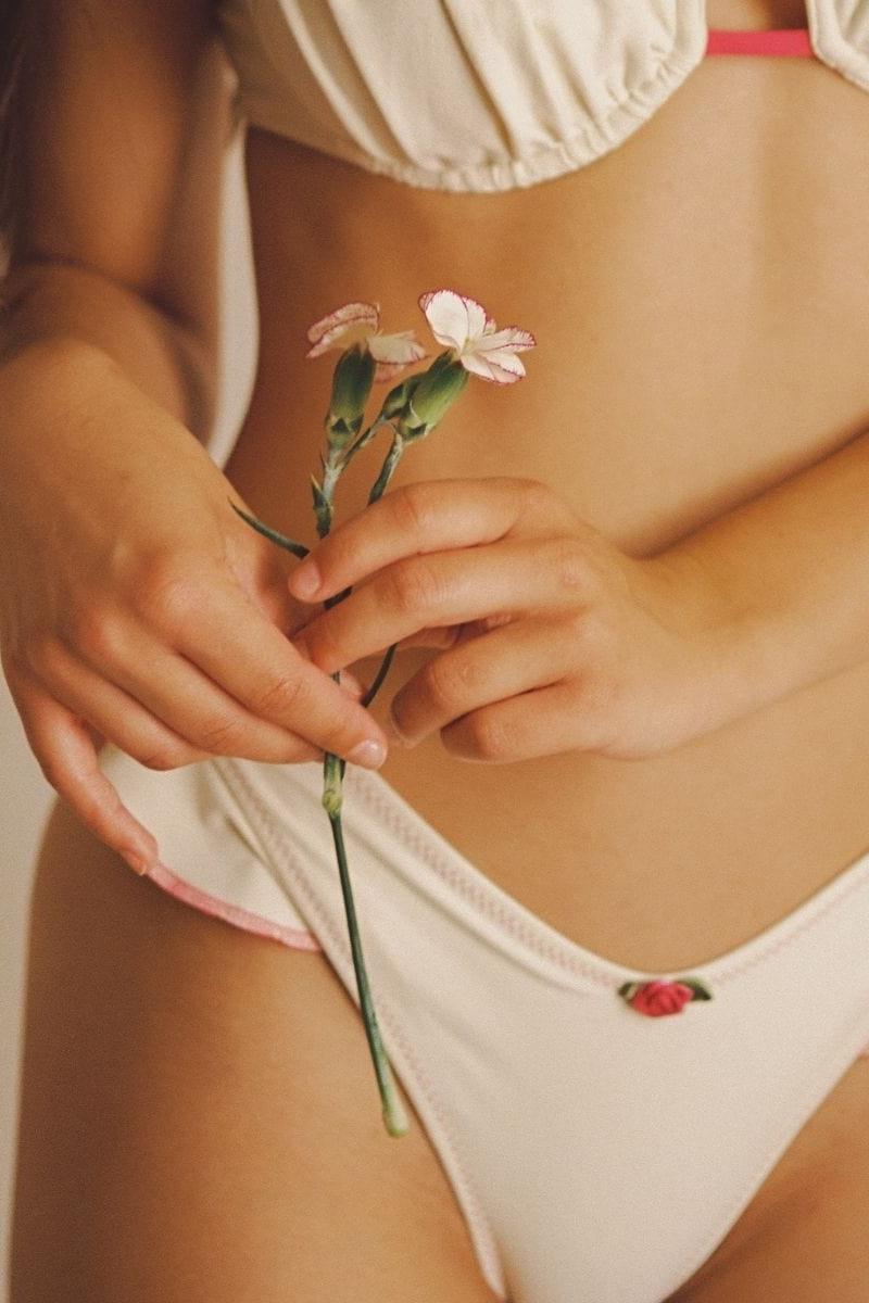 Cream bikini bottom with raspberry binding at waistband and small floral embroidery detail at hip.