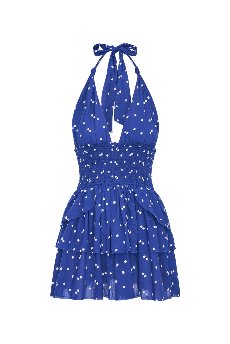 Low-cut navy blue convertible halter dress with hand-painted star print all over and a smocked waist, ties in a generous bow at the neck and can be crossed at front with a flared skirt with two ruffled tiers.