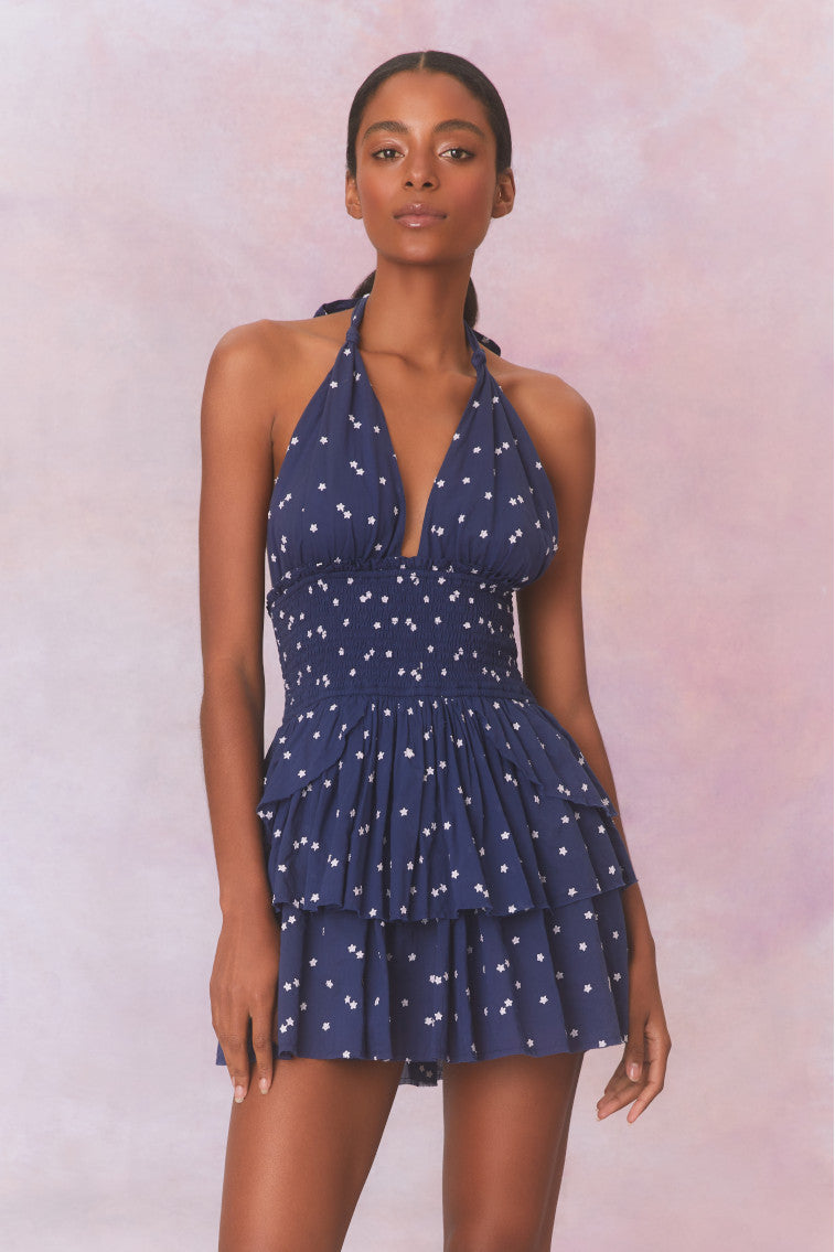 Low-cut navy blue  convertible halter dress with hand-painted star print all over and a smocked waist, ties in a generous bow at the neck and can be crossed at front with a flared skirt with two ruffled tiers.