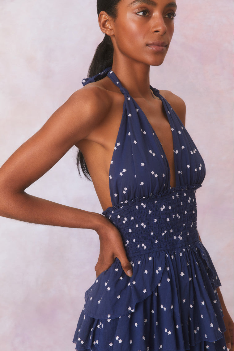 Low-cut navy blue  convertible halter dress with hand-painted star print all over and a smocked waist, ties in a generous bow at the neck and can be crossed at front with a flared skirt with two ruffled tiers.