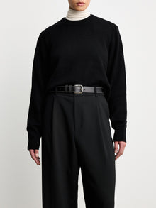 Model wearing D√©hanche Louison black leather belt with white stitching and silver buckle, styled with black trousers and a black sweater