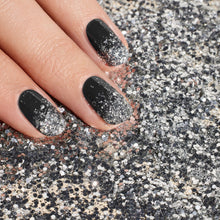 A hand with black and silver ombré nails, enhanced by Manucurist's Glitters Duo Silver  Mirror, rests on a surface dusted with loose silver and black glitter.
