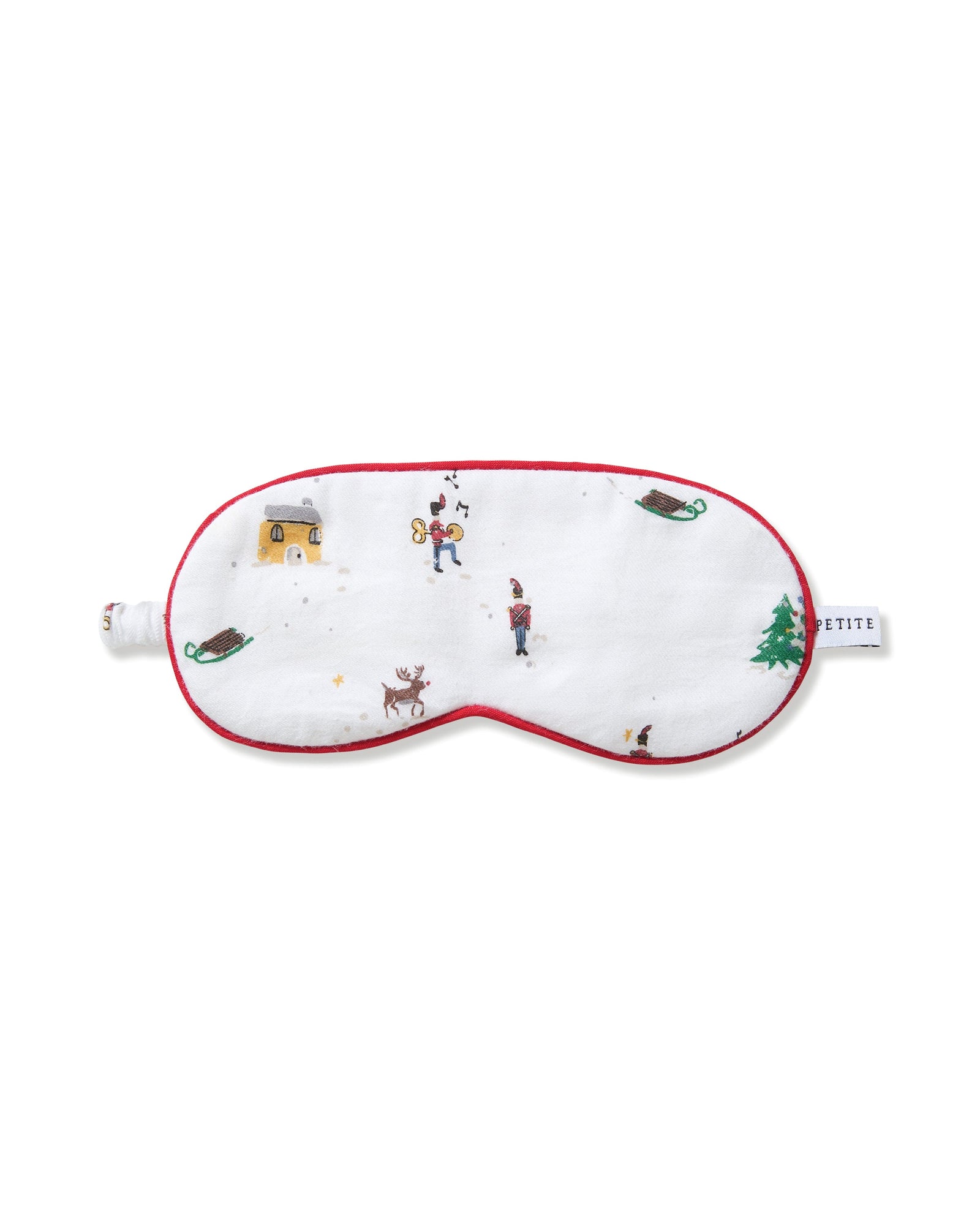 The Kid's Twill Sleep Mask in Holiday Town is a white mask with red trim, decorated with winter scenes of people, a reindeer, a house, a sled, and snowy trees. A small white tag is attached on the right side.