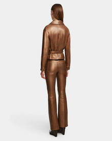 A person with straight brown hair, seen from behind, wears the Rudsak ARIELLE - 8124052 Antique Bronze women’s peplum jacket with matching flared pants and black shoes against a plain white background.