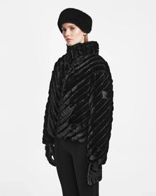 A woman stands poised in the ANASTASIA - 8124804 Black luxury winter coat by Rudsak, a sleek black velvet puffer.