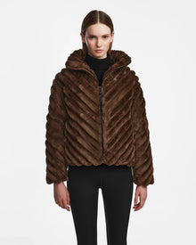 A woman faces forward wearing the Rudsak ANASTASIA - 8124804 Espresso, a textured brown faux fur zip-up jacket with a hood and black fitted pants, styled against a plain white background.