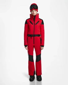 A person faces forward wearing the Rudsak ARLEY - 8124717 Flame Red fitted women’s ski suit with black accents, black gloves, boots, and ski goggles on their head. Set against a plain white background. Features integrated RECCO rescue technology.