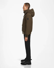 A person stands in profile against a white background, wearing the Rudsak ASH - 6124599 Army mens down bomber jacket for an urban style look, paired with black pants and black boots.