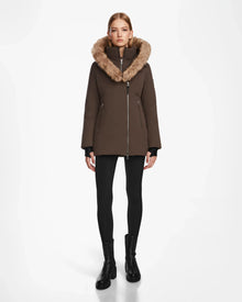 A woman faces forward against a white background, wearing the Rudsak AURORE - L123561 Espresso fitted down parka with fur trim, paired with black leggings and ankle boots.