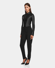 A woman with straight brown hair and a neutral expression poses against a plain background, wearing a fitted black collared button-up top, Rudsaks CARDI - 8524561 Black pull-on trousers with a patent stripe, and black heels.