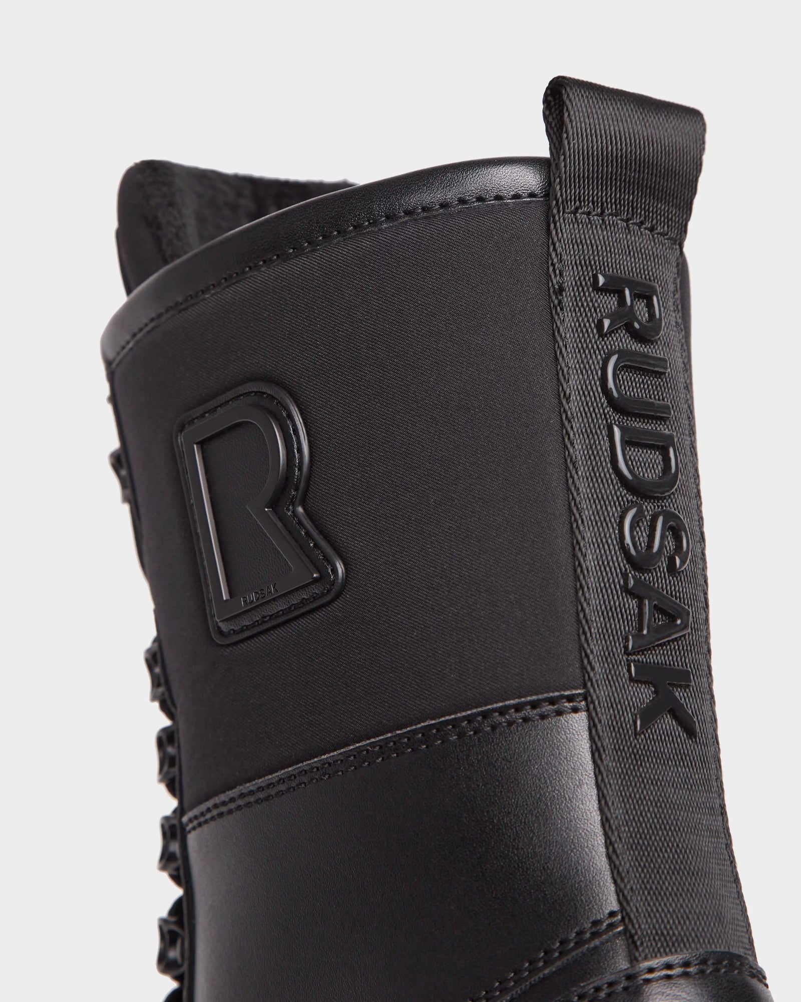 Close-up of the black Rudsak DAMIEN - M222500 men’s winter boot, showing the embossed logo on the pull tab and a raised R emblem. The insulated boot features matte, textured, weather-treated leather.