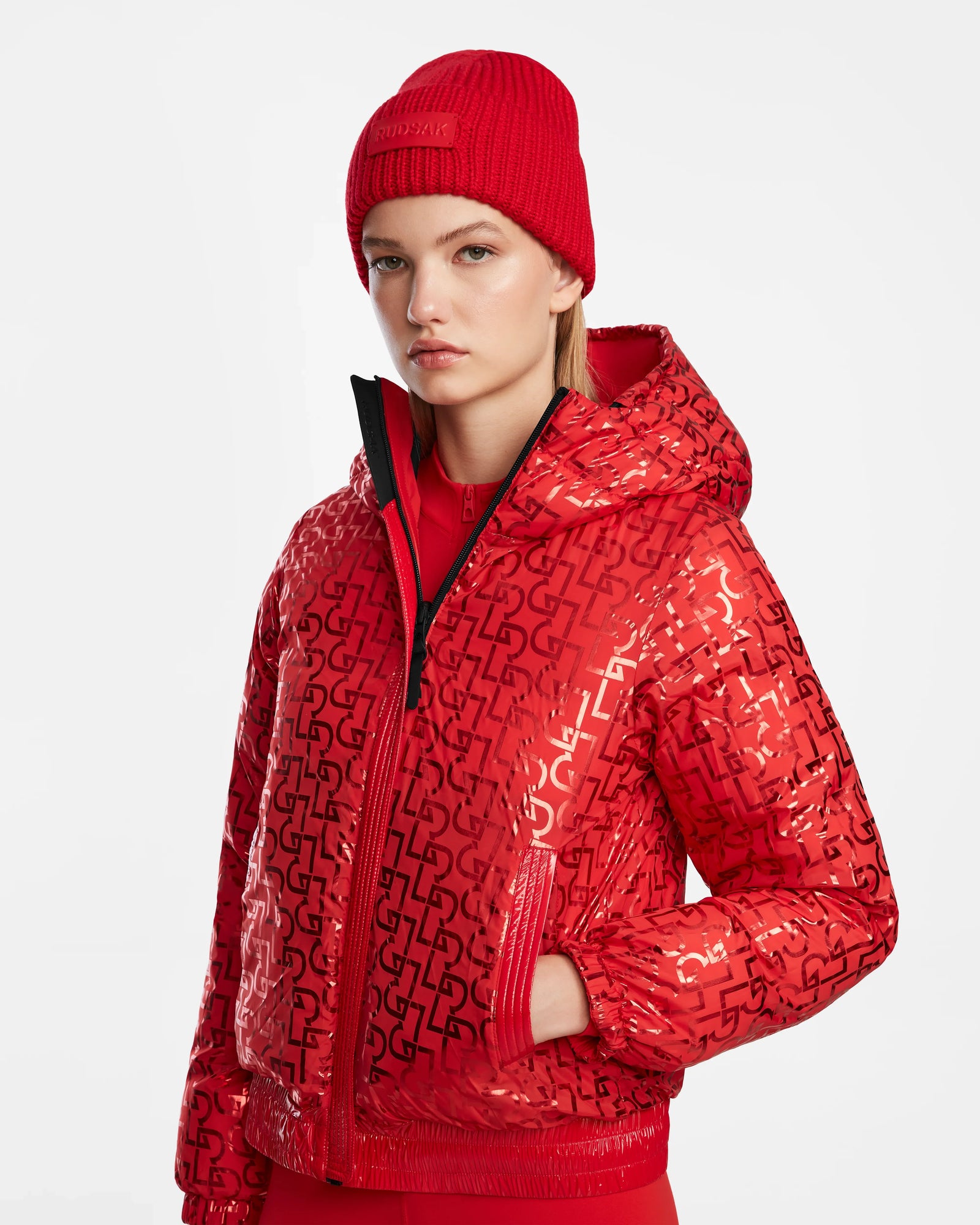 A woman in the Rudsak DANI M - 8124539 Flame Red cropped bomber jacket, matching red beanie, and red pants stands against a white background, creating a bold après-ski statement look.