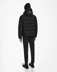 A person faces away, wearing the Rudsak DEMIAN M - M123507 Black mens down puffer jacket with a hood, black pants, black shoes, and a black knit beanie against a plain white background.