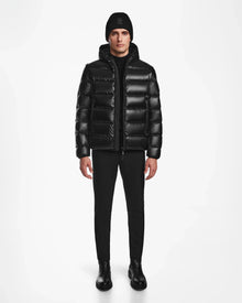 A person stands facing forward against a white background, wearing the Rudsak DEMIAN S-R - M123505 Black mens down puffer jacket with RDS-certified down, paired with black pants, boots, and a knit beanie.