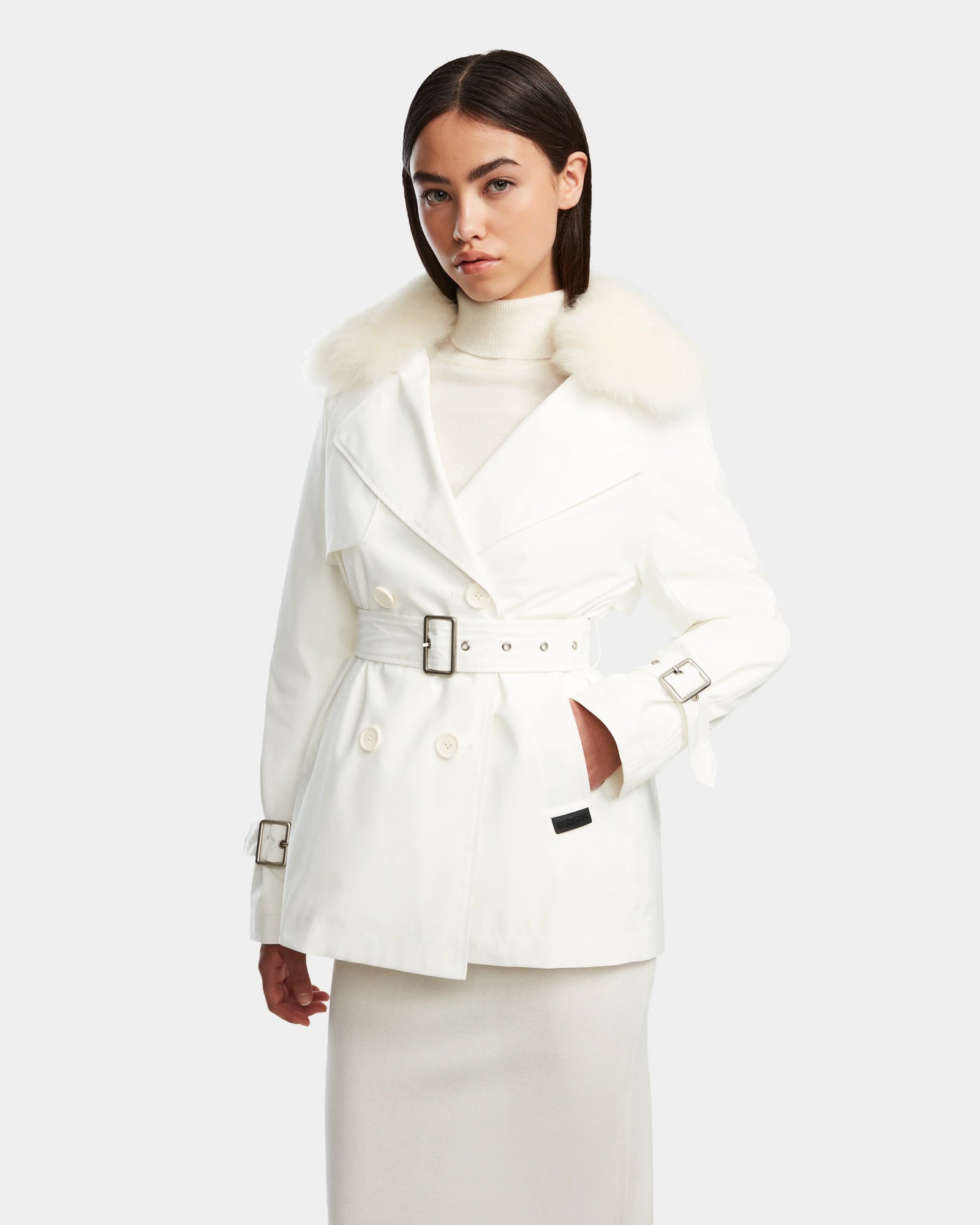 A woman models the Rudsak ELENOR - 8124707 Iceland white trench coat with a shearling collar over a white turtleneck and long skirt, standing against a plain light background.