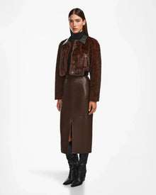 A woman stands against a white background wearing Rudsaks EVELYN - 8124791 Espresso, styled with a brown faux fur jacket, long brown leather skirt with front slit, black turtleneck, and black knee-high boots.