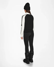 A person faces away, wearing the Rudsak FANNY - 8524506 Black jacket, layered for winter with black leggings, boots, and a beanie, all set against a plain white background.