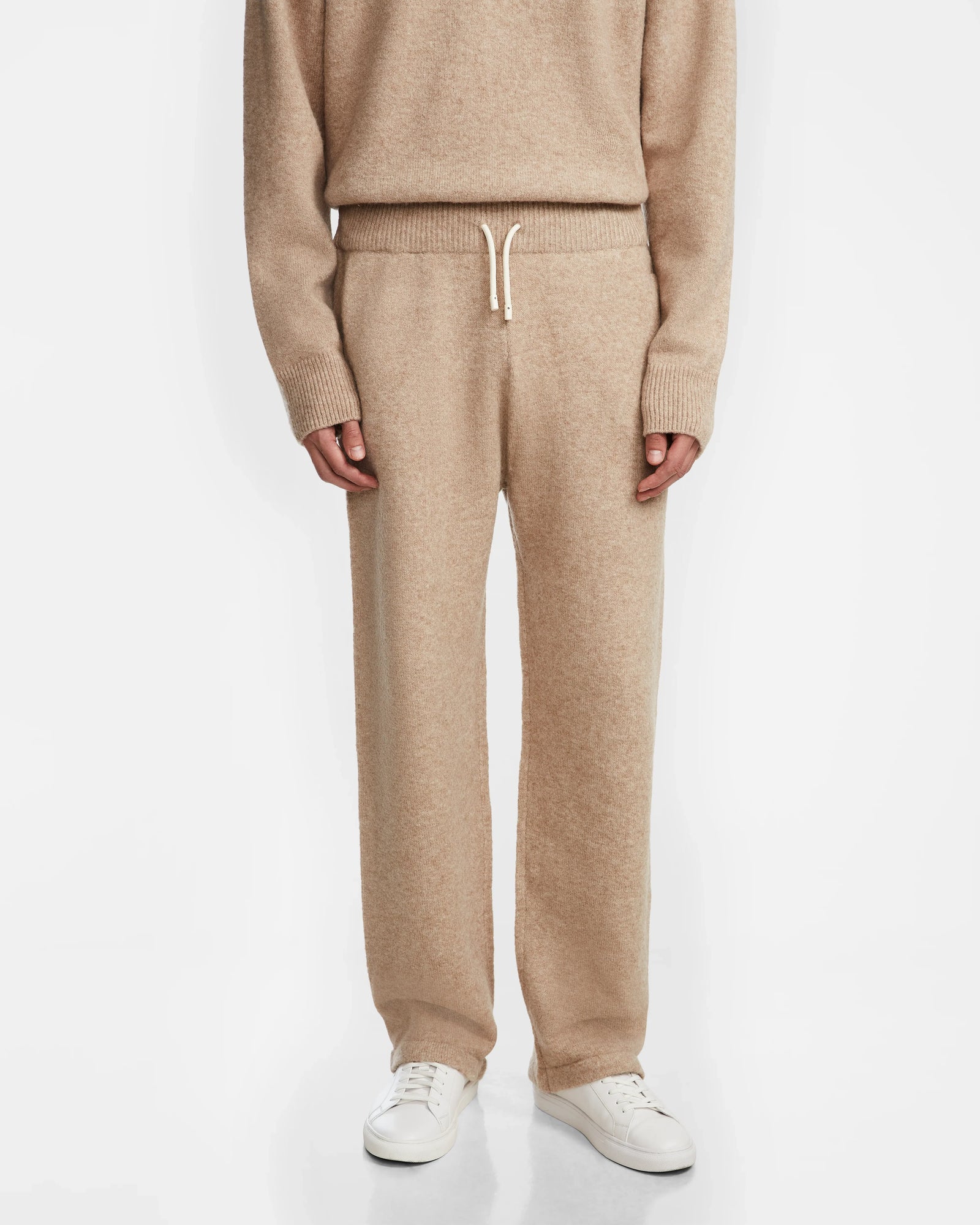 A person models the Rudsak GEIGER - 9524512 Camel M knit sweater and relaxed lounge pants with white sneakers, standing against a plain white background for a cozy and relaxed look.