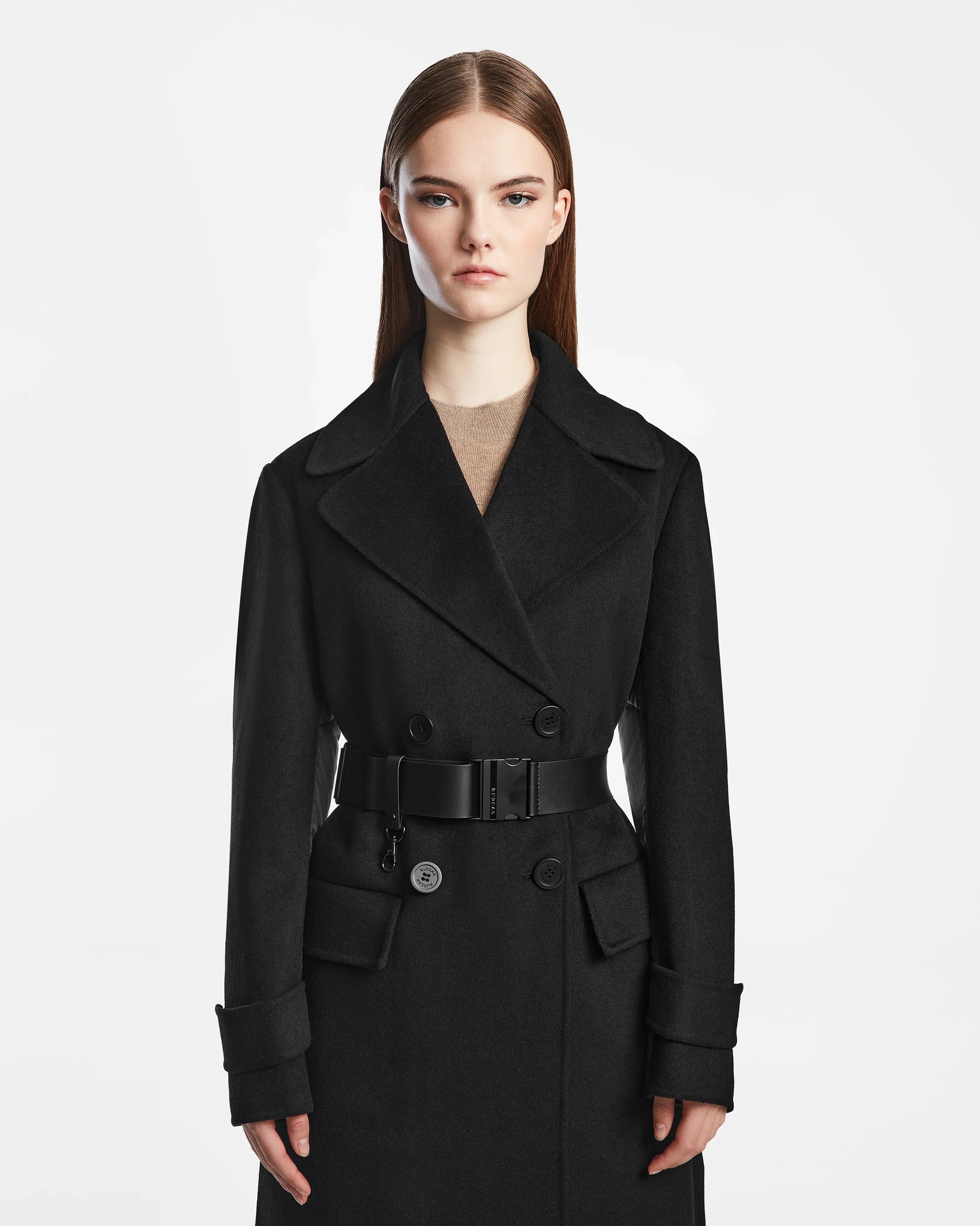 A woman with straight brown hair models the Rudsak IVE - L124560 Black wool blend long coat, a double-breasted style with a wide belt, standing against a plain white background and looking at the camera with a neutral expression.