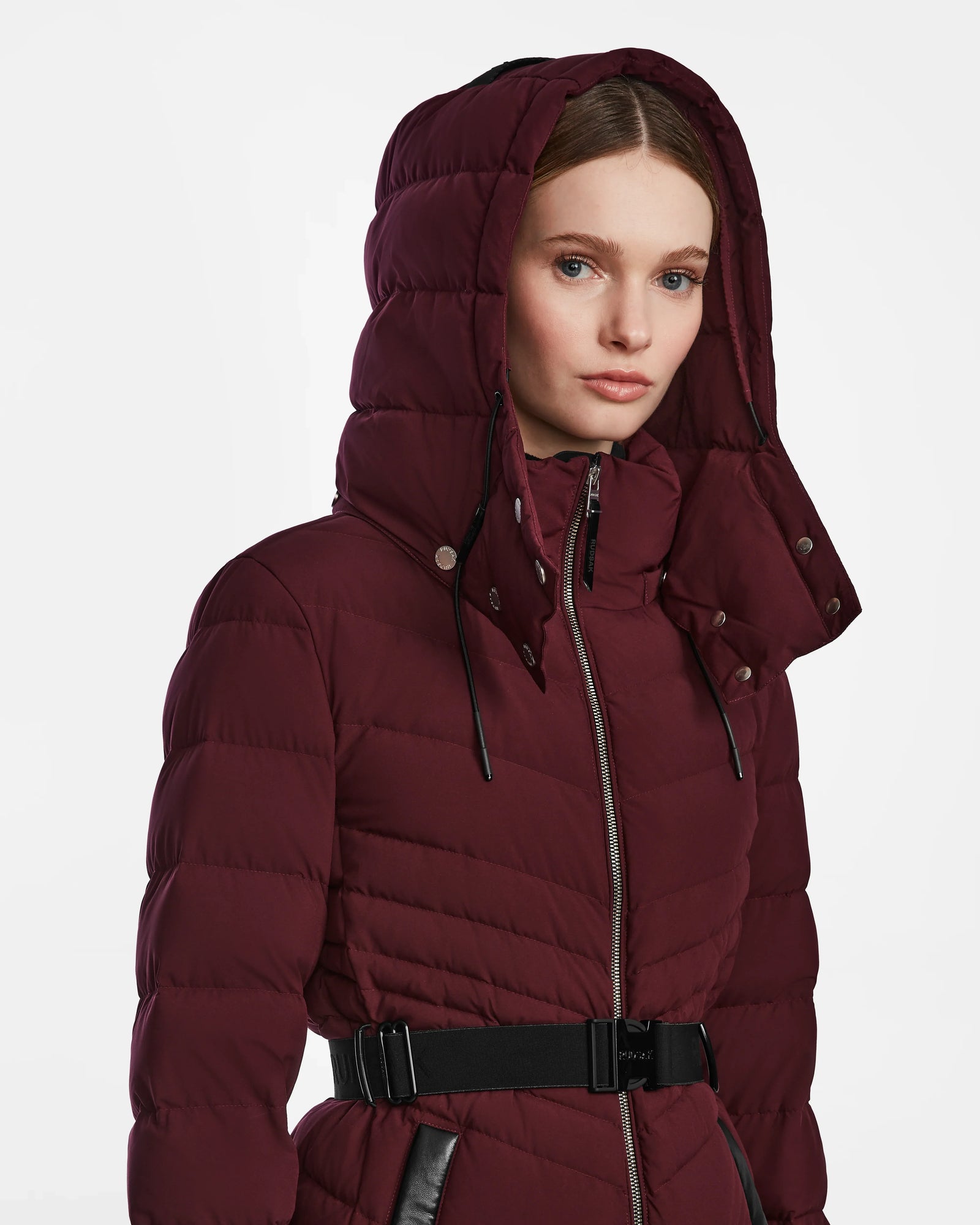A woman wearing the Rudsak MALAYA M - L123554 Wine herringbone hooded jacket with a zipper and black belt, looking forward against a plain white background.