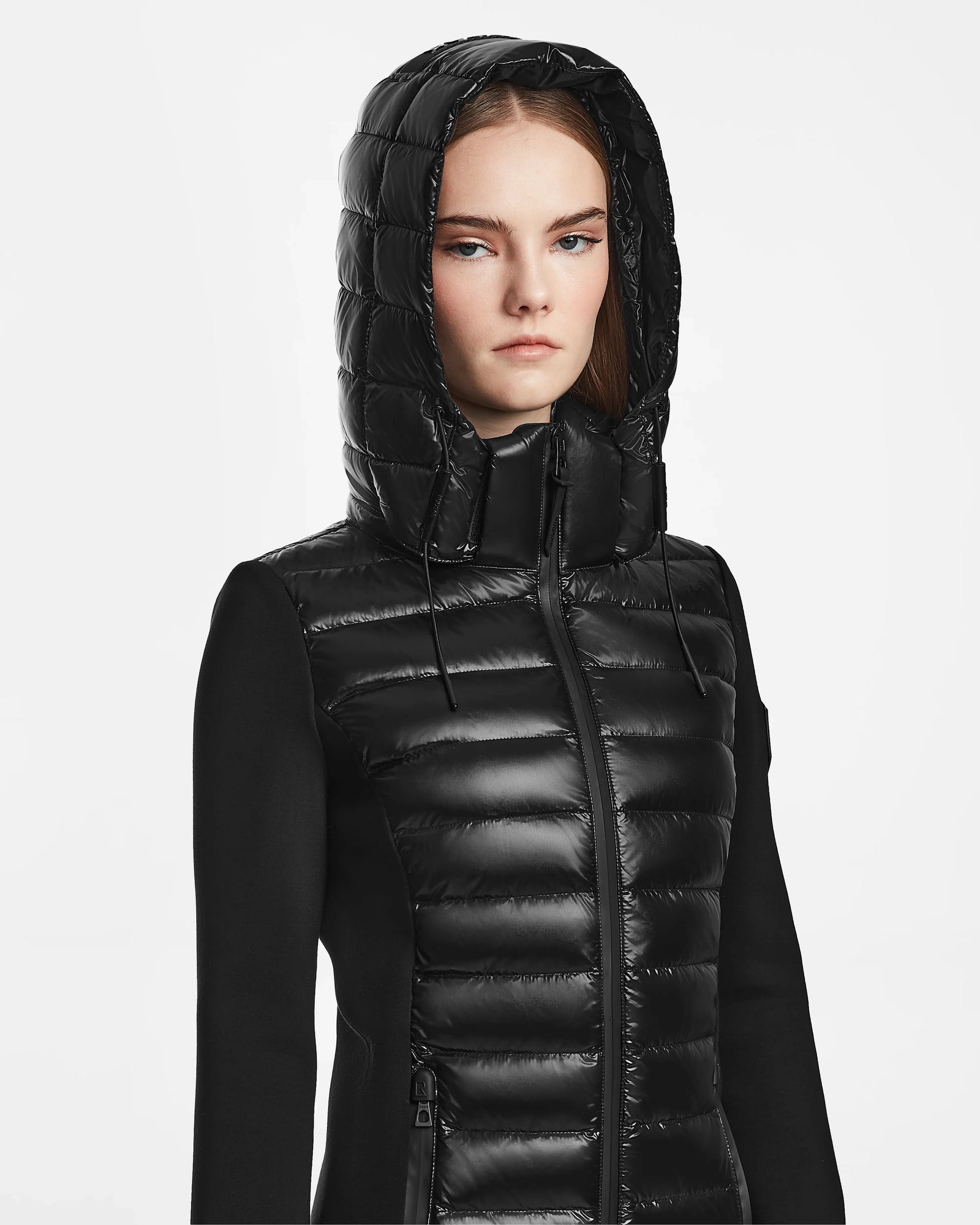 A woman wears the Rudsak MARRY - L121003 BLACK puffer jacket with the hood up, looking directly at the camera against a plain white background.