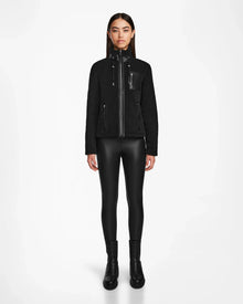 A woman faces forward against a white background, wearing the Rudsak MILANA - 8524604 Black zip-up jacket with vegan leather details, black faux leather leggings, and black ankle boots.