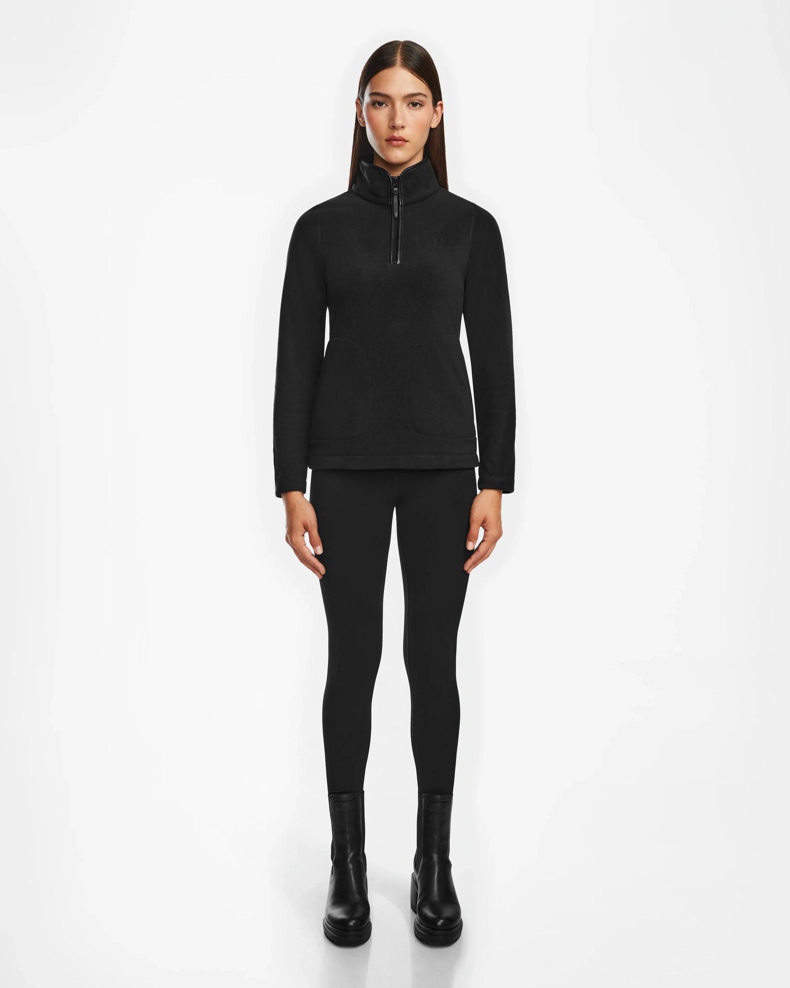 A woman with straight brown hair wears the Rudsak ORCHID - 8524616 Black women’s half-zip pullover with vegan leather trims, black leggings, and ankle boots, standing facing forward against a plain white background.