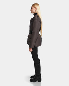 A woman with long blonde hair is seen in profile wearing the Rudsak PAOLA - 8124547 Grey womens down blazer with a belt, styled with black pants and boots against a plain light background.