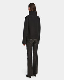A person faces away, wearing Rudsaks PARMI - 8524608 Black womens knit turtleneck sweater and flared black leather pants, set against a plain white background.