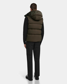 A man faces away in black pants, shoes, and a black long-sleeve shirt layered with the Rudsak REN M - 9123512 Army M olive weather-resistant puffer vest with RDS-certified down. RUDSAK is printed on the hood. Background is plain white.
