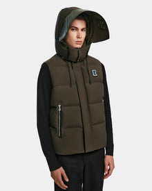A man models the Rudsak REN M - 9123512 Army M puffer vest, weather-resistant with a high collar, large hood, R logo on the chest, and RDS-certified down insulation over a black shirt against a light gray background.