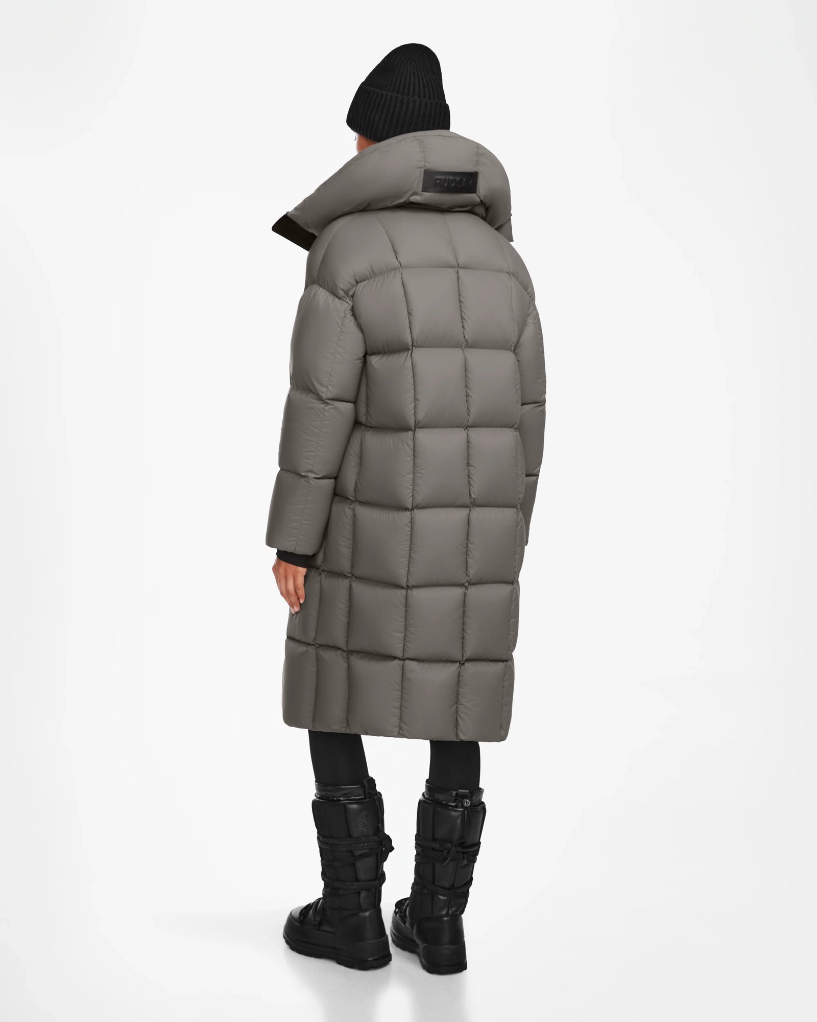 A person in the Rudsak SASH - 8124536 Light Grey long down puffer coat, black pants, black boots, and a black knit beanie stands facing away against a plain white background.