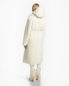 A person with light hair faces away, wearing Rudsaks TINA - 8123578 Iceland ivory textured womens trench coat with a removable hooded bib, matching pants, and chunky off-white boots against a plain white background.