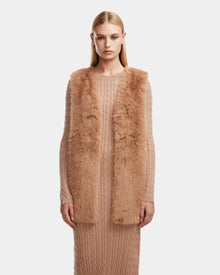 A woman with straight blonde hair models the Rudsak YOLANDA - 8124790 Camel long cable-knit dress, styled with a women’s faux fur vest and vegan leather belt—perfect for fall and winter—against a plain white background.
