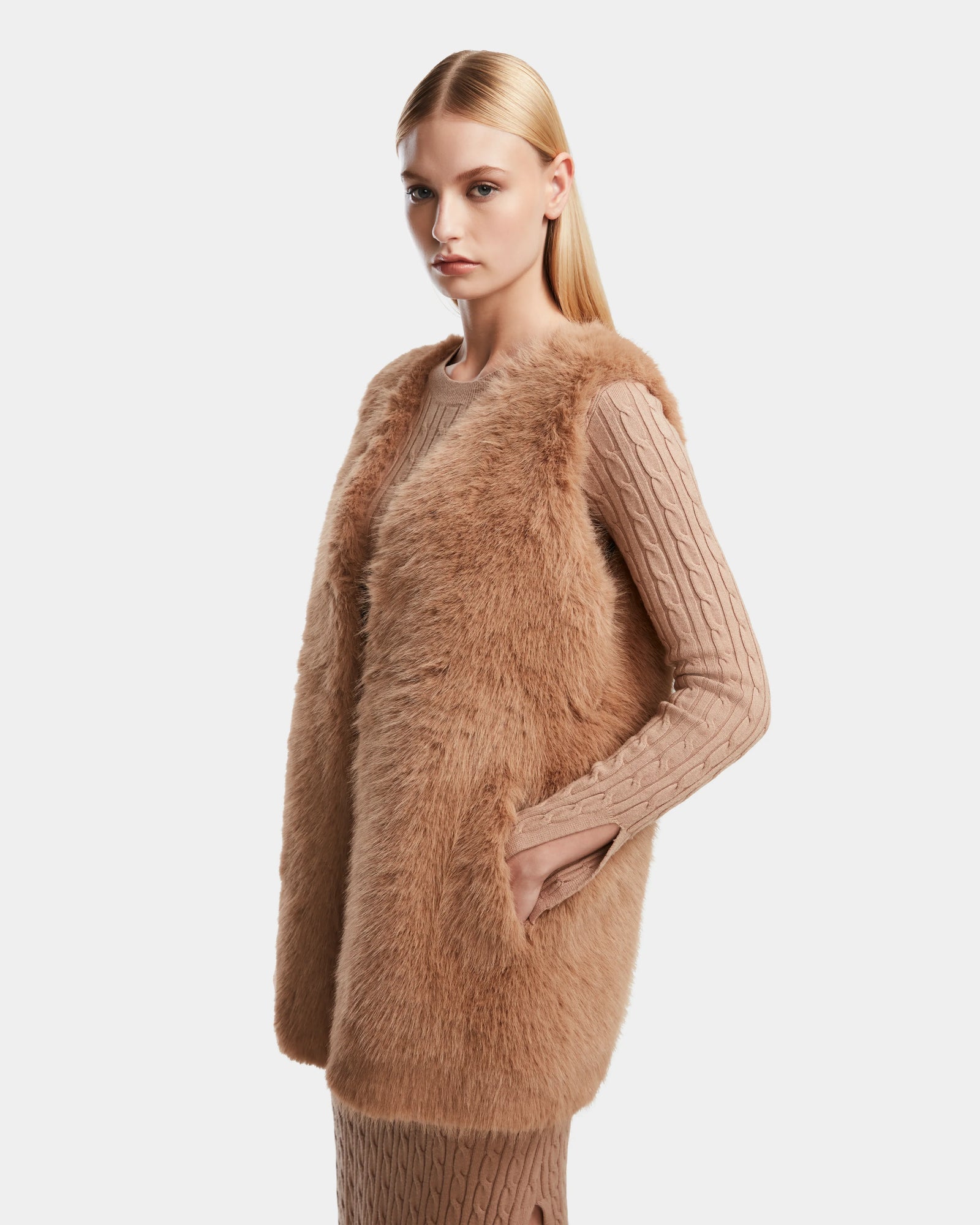 A woman models the YOLANDA - 8124790 Camel faux fur vest by Rudsak over a coordinating knit sweater dress, styled with a vegan leather belt—an ideal choice for your fall and winter wardrobe.