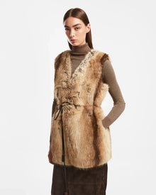 A woman models the Rudsak YOLANDA - 8124790 Mocha faux fur vest over a taupe turtleneck and dark brown skirt with a vegan leather belt, set against a white background—a stylish fall/winter look.