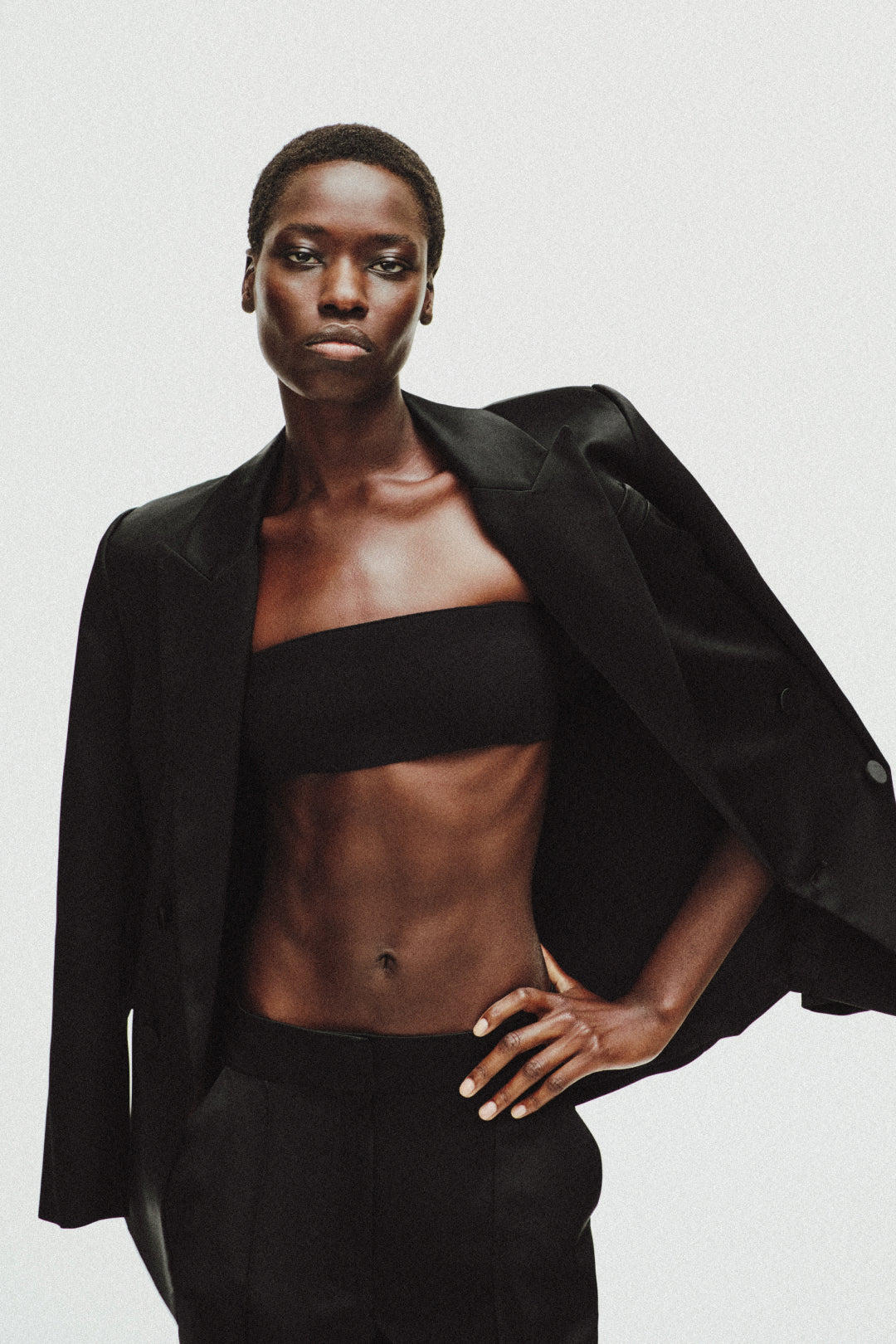 Black satin blazer with sharp lapels and button closure worn open over black crop top.