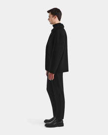 A man stands in profile facing left, wearing the Rudsak AIDEN - 6125558 Black men’s wool-blend coat with black pants and shoes, set against a plain white background.