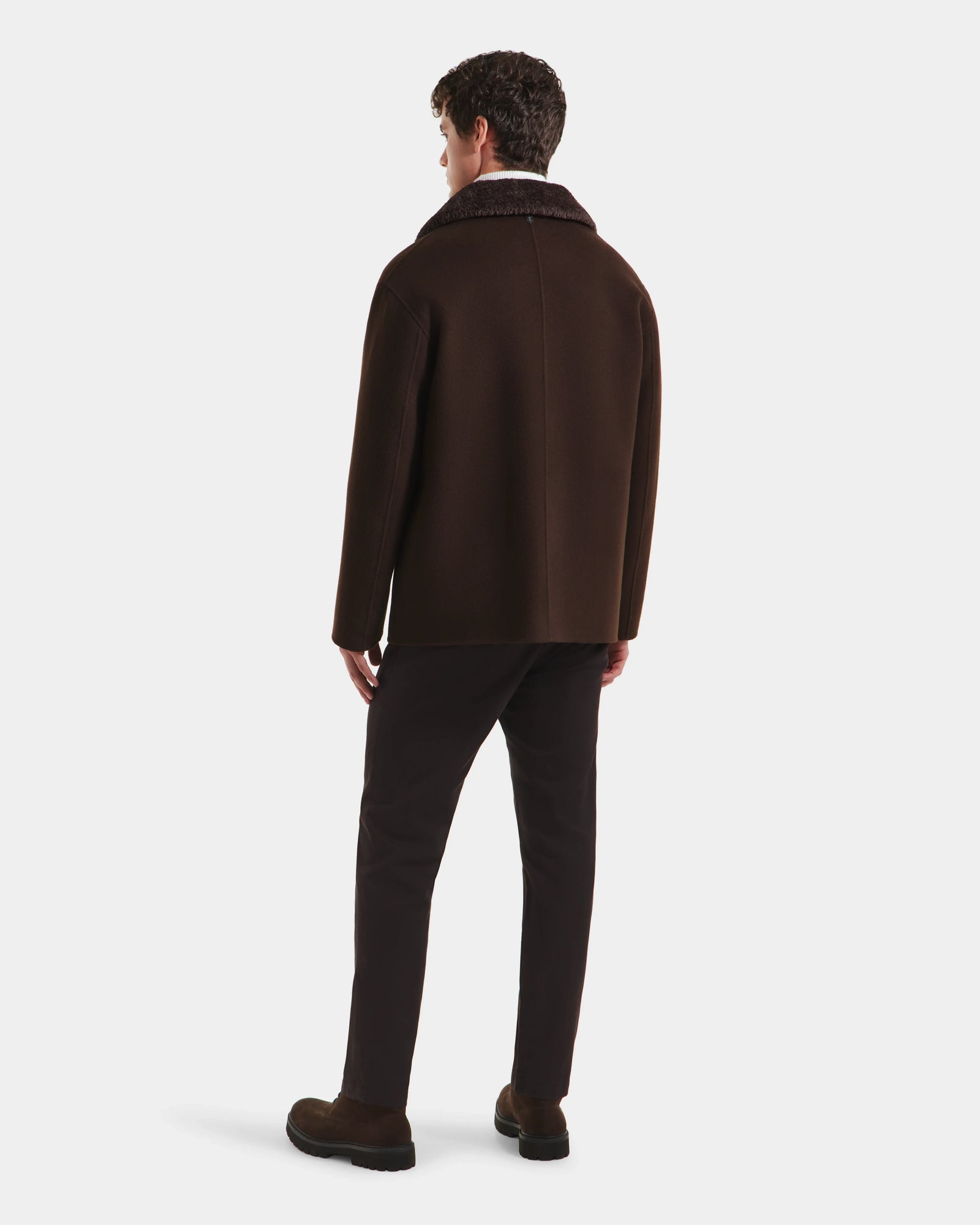 A man faces away, wearing the Rudsak AIDEN - 6125558 Espresso mens wool-blend coat with a textured collar, paired with dark trousers and brown shoes against a plain white background.