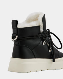 A close-up of the Rudsak ALEXEY L - L225518 Black women’s leather boot featuring black lace-up detail, plush white wool lining, and a thick white sole, shown from the back and side against a plain background.
